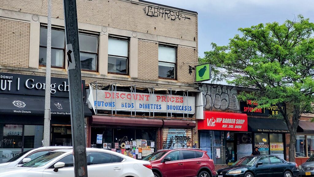 Storefronts along Harvard Avenue in Allston Village, with a bubble tea shop, donut shop, barber shop and street trees