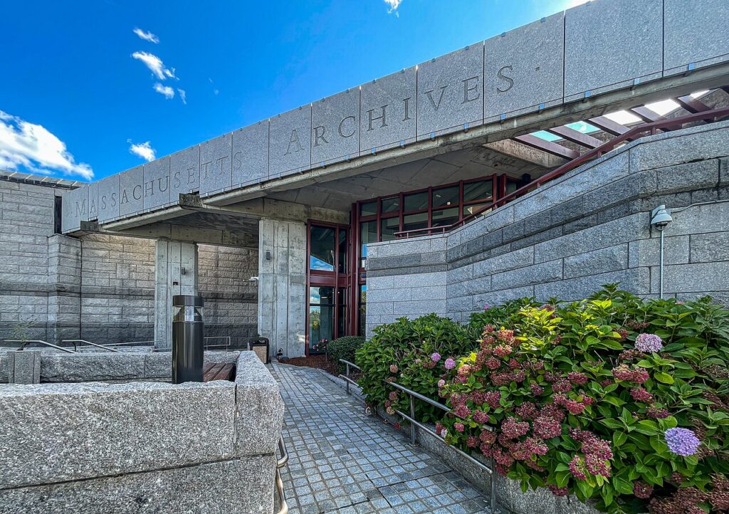 Granite entrance of the Massachusetts Archives and Commonwealth Museum building at Columbia Point in Dorchester, with hydrangeas in bloom under a blue sky