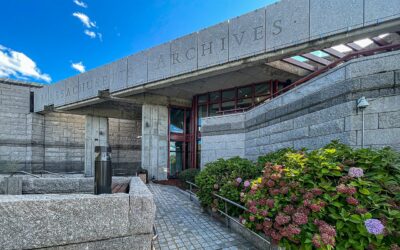 Granite entrance of the Massachusetts Archives and Commonwealth Museum building at Columbia Point in Dorchester, with hydrangeas in bloom under a blue sky
