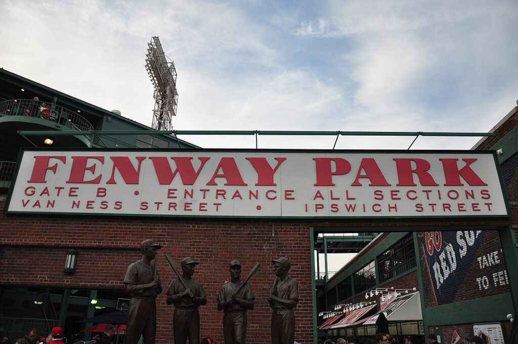 Gate B entrance of Fenway Park in Boston with the red FENWAY PARK sign and The Teammates bronze statues on Van Ness Street