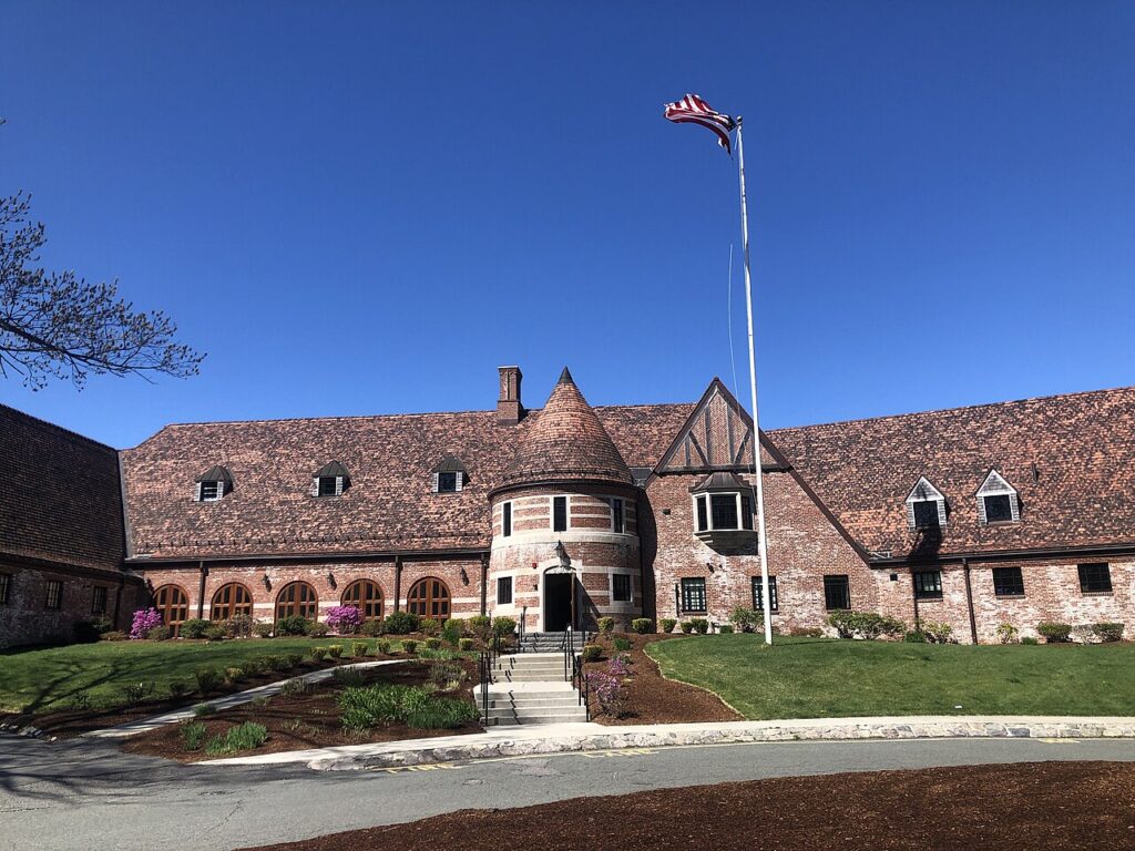Brick Tudor-style clubhouse of George Wright Golf Course in Hyde Park, Boston, with an American flag under a clear blue sky