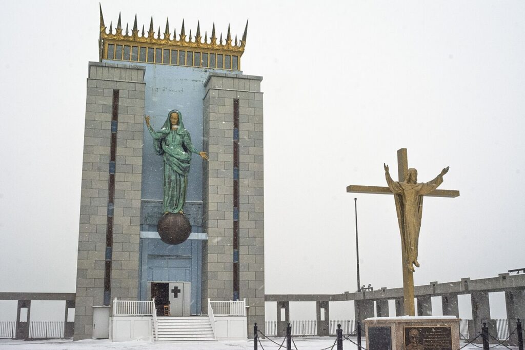 Front of the Madonna Queen of the Universe Shrine in East Boston, with the copper Madonna statue standing on a globe beneath the gold crown, in light snow