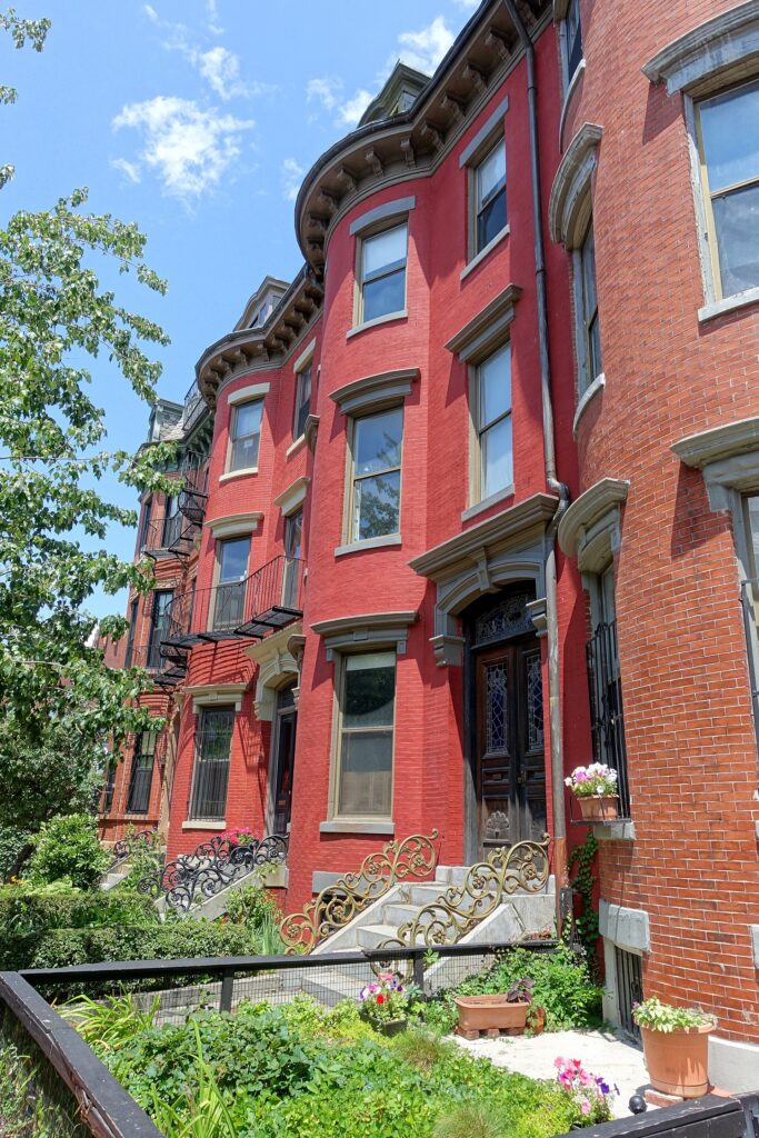 Red-painted Victorian bowfront rowhouses with ornate iron stoop railings on West Concord Street in the South End