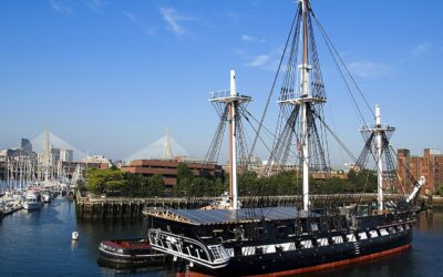 USS Constitution moored at the Charlestown Navy Yard under a clear blue sky, with the Zakim Bridge visible in the background